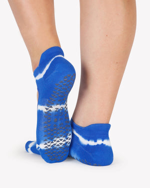 A close up photo of a woman's feet wearing blue and white tie-dye socks with grip
